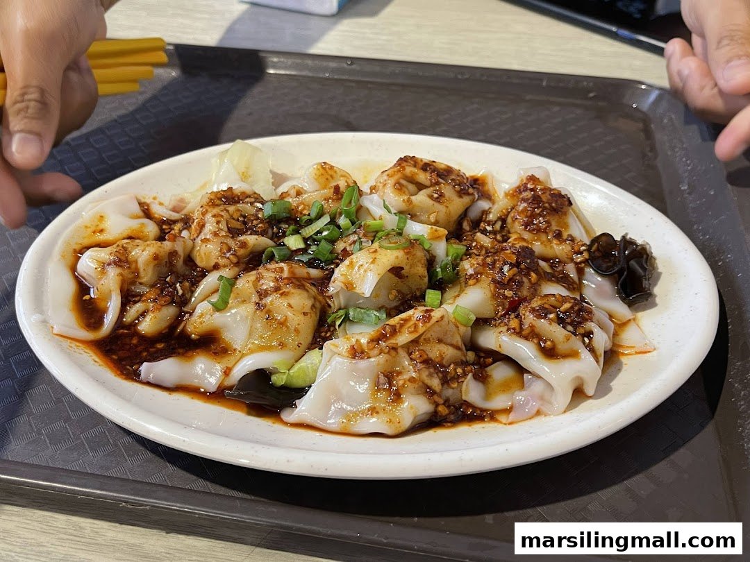 A close-up of a plate of spicy wontons or dumplings, garnished with spring onions and chili oil.