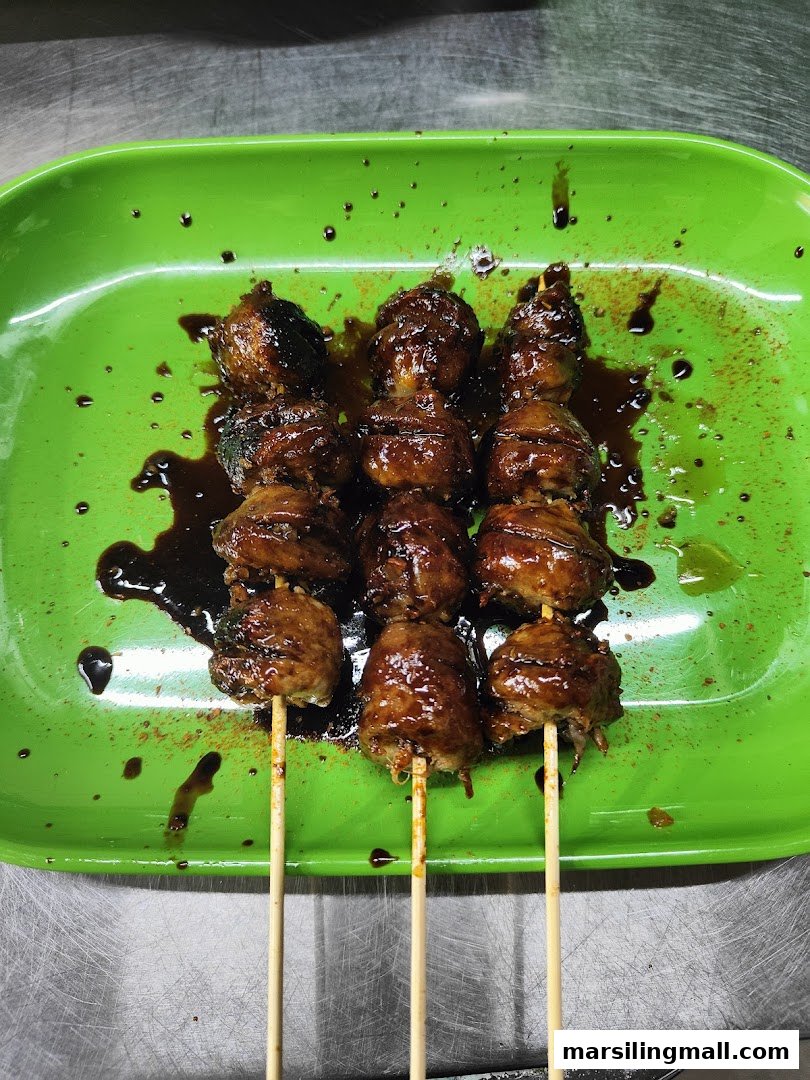 Three skewers of glazed meatballs or satay served on a vibrant green plate.