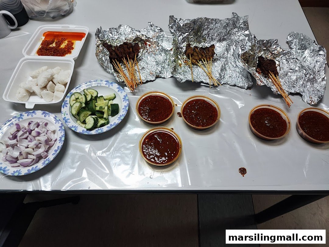 A table laden with satay skewers, peanut sauce, rice cakes, sliced onions, and cucumbers.