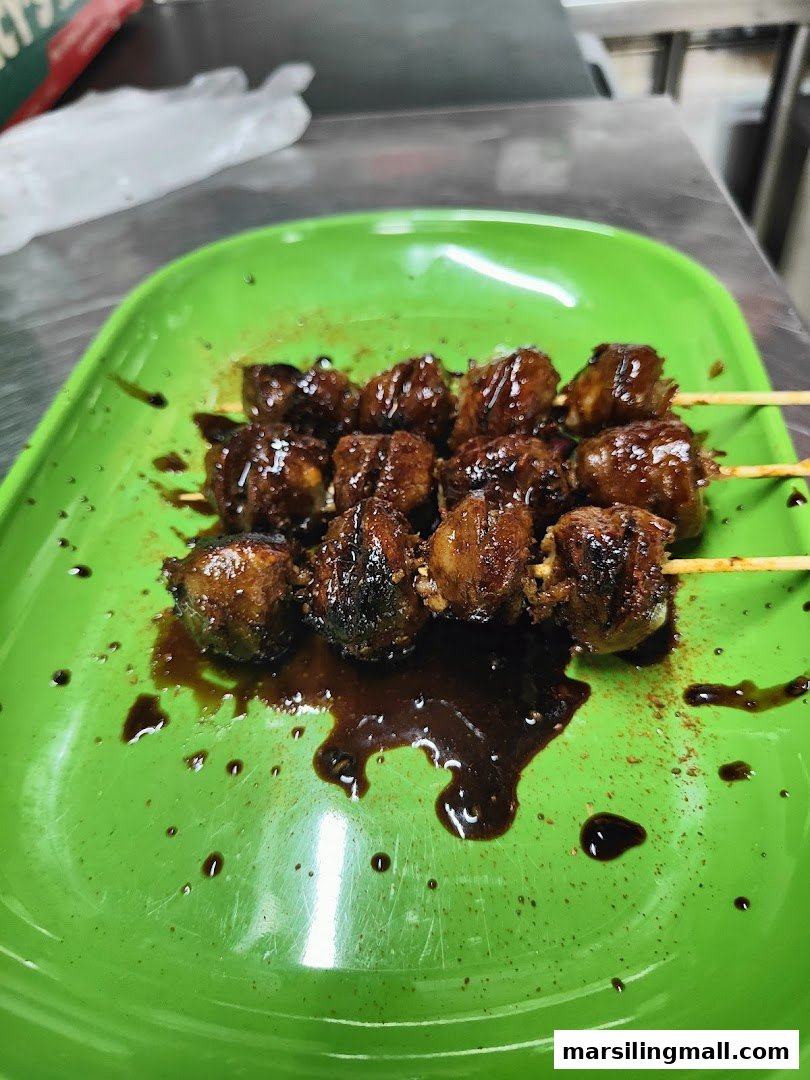 A vibrant green plate holds several skewers of glazed, grilled meat or meatballs, glistening with sauce.