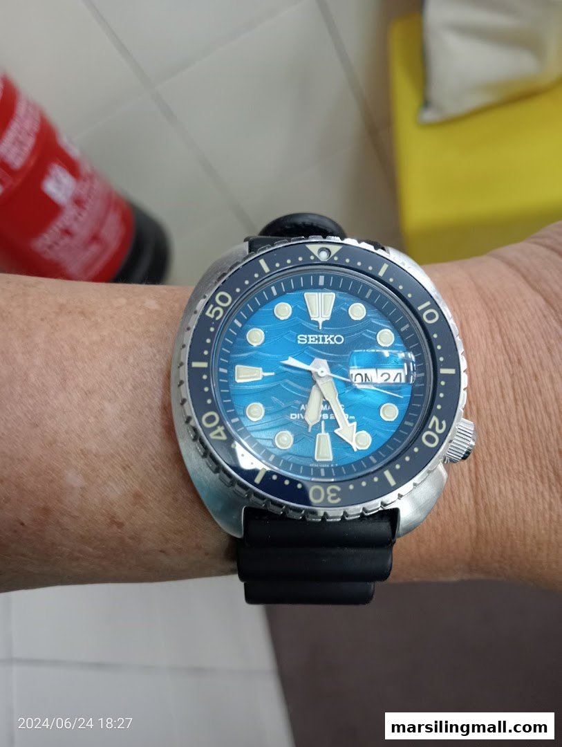 A person wears a blue-faced Seiko dive watch with a black strap on their wrist.