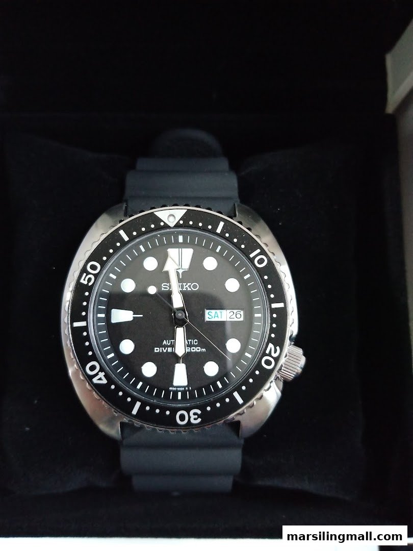 A close-up of a black Seiko automatic diver's watch with a rubber strap in its box.