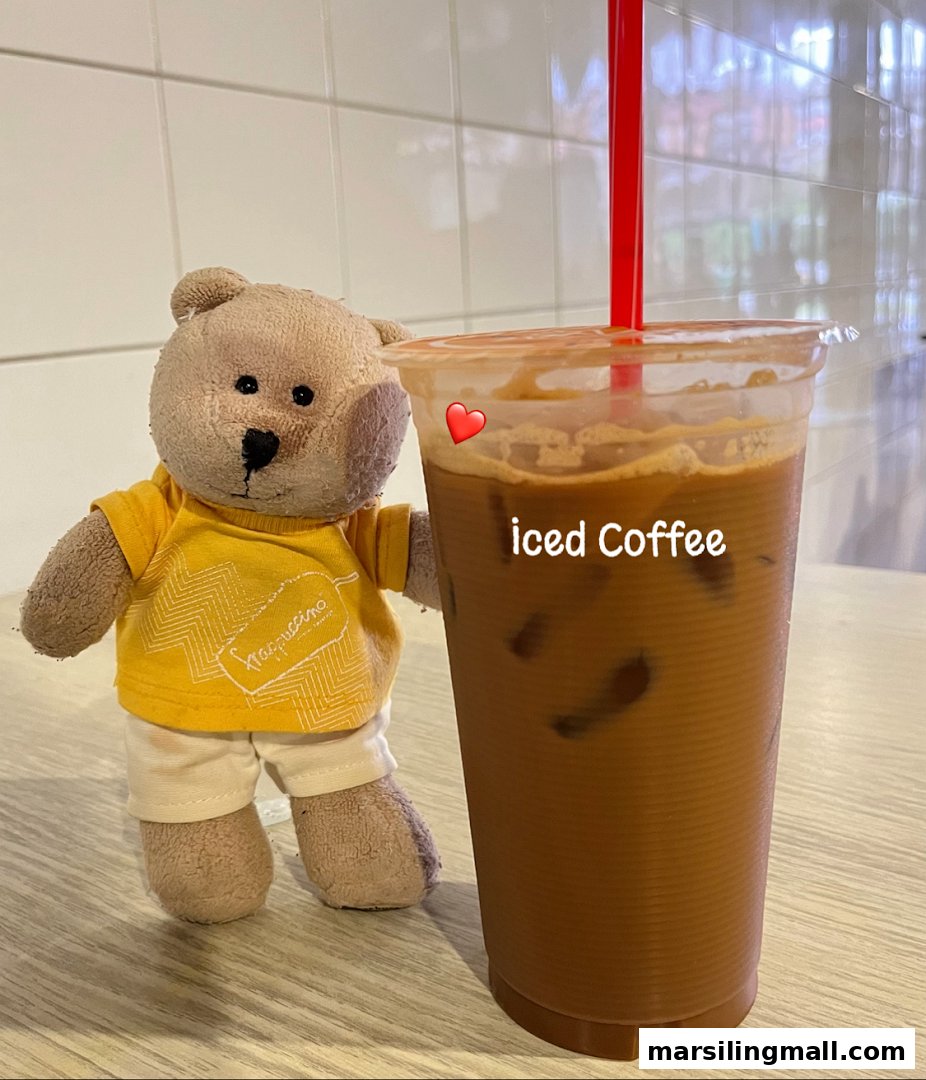 A cute teddy bear stands beside a tall glass of iced coffee with a red straw.