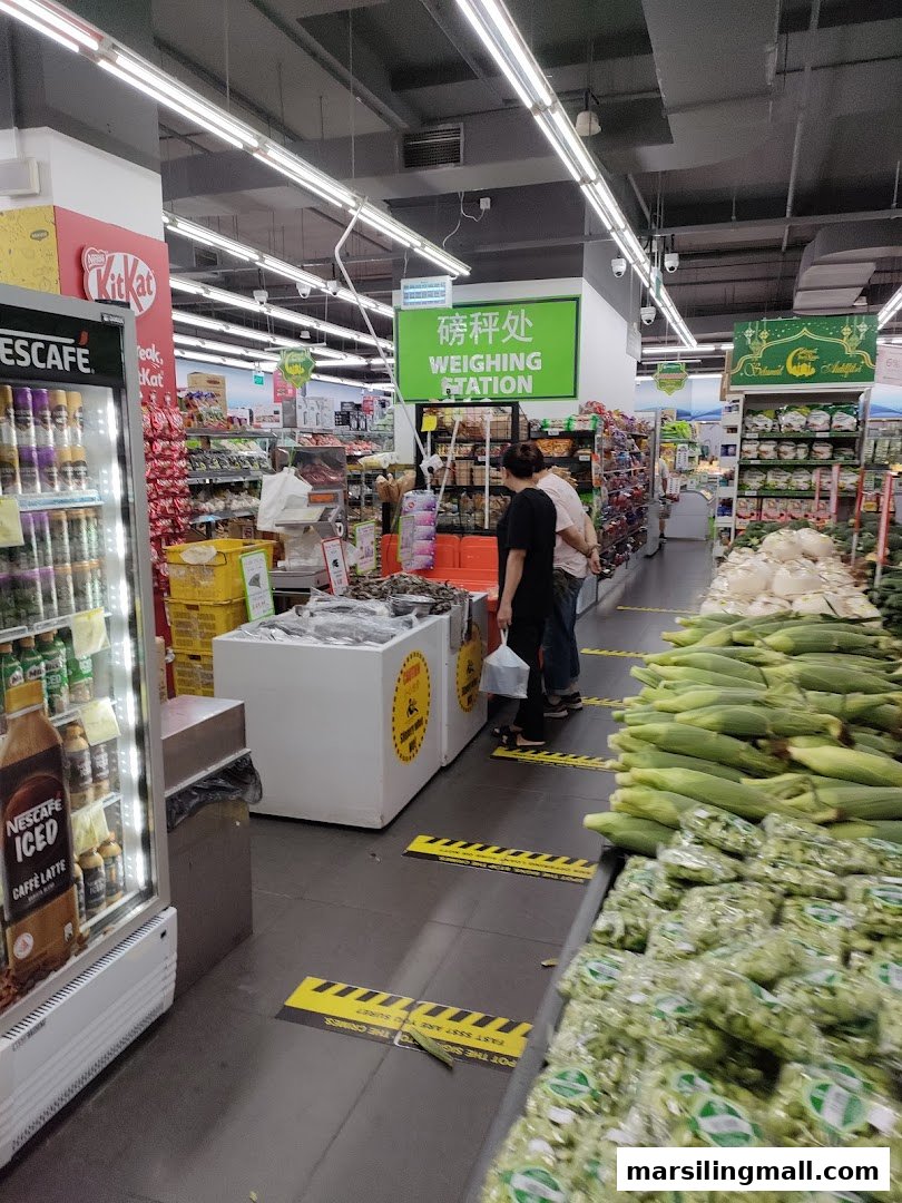 A bustling supermarket aisle at Sheng Siong, featuring fresh produce, a weighing station, and various groceries.