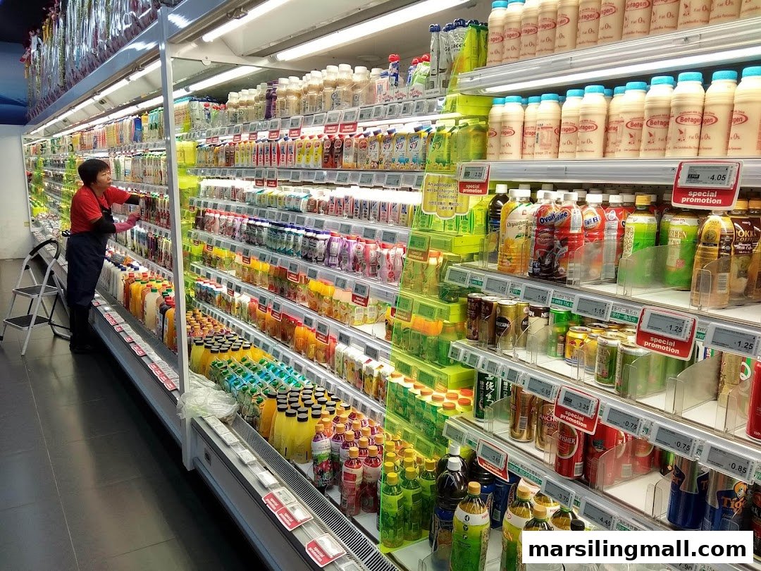 A supermarket staff member stocks shelves filled with various beverages and dairy products.
