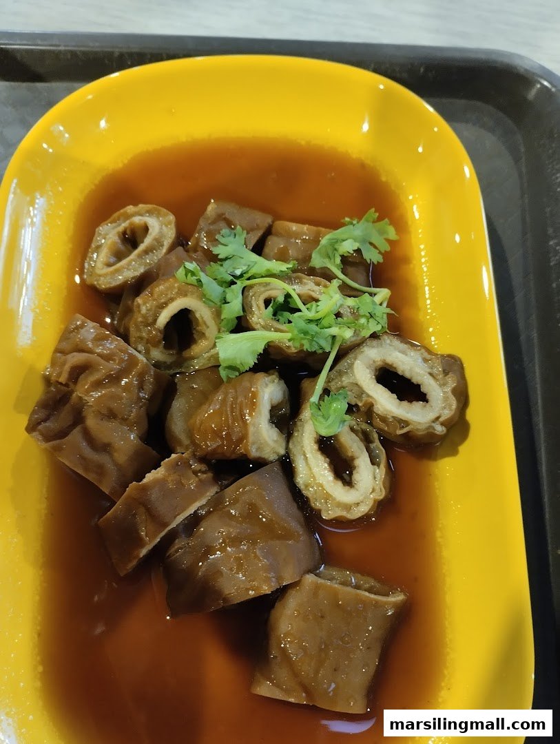 A vibrant yellow plate holds braised pig intestines or offal, garnished with fresh cilantro in a rich brown sauce.