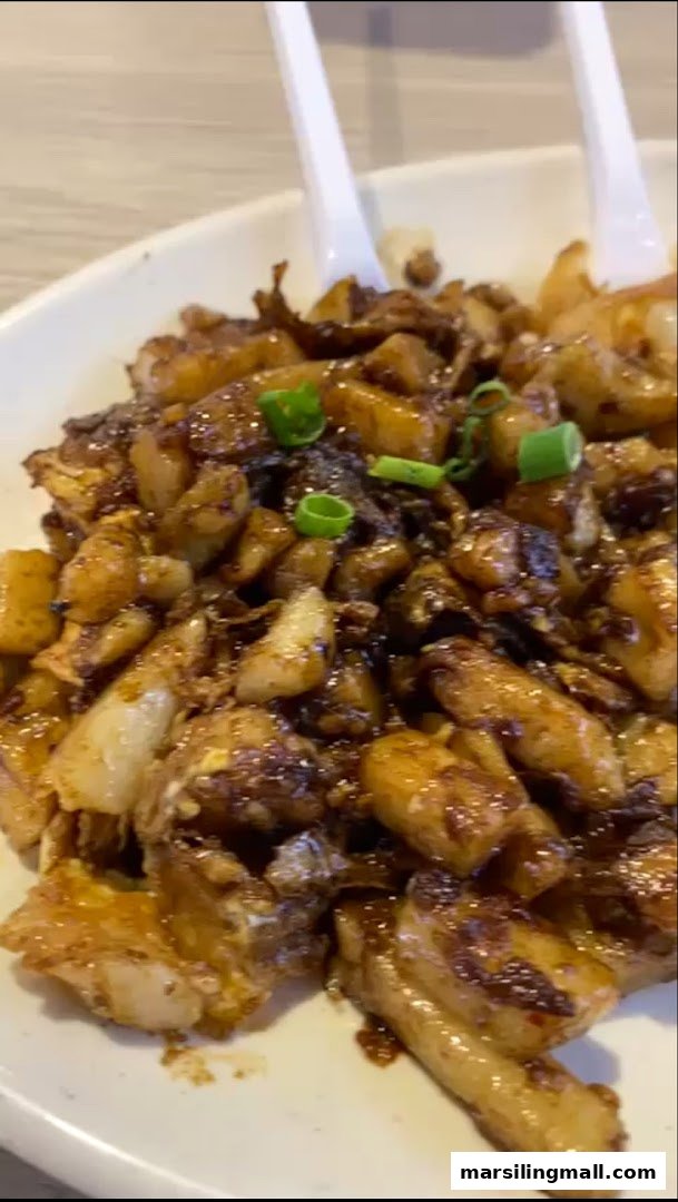 A close-up of a plate of dark fried carrot cake garnished with chopped spring onions.