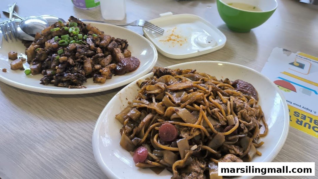 Two plates of delicious local dishes, including fried carrot cake and char kway teow, on a table.