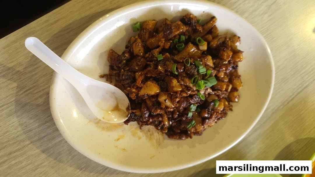 A plate of dark fried carrot cake, garnished with spring onions, and a white spoon.