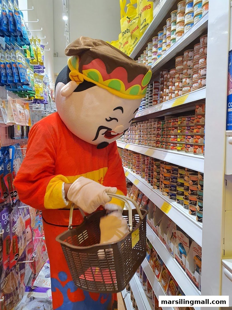 A mascot in a traditional costume holds a shopping basket while browsing shelves stocked with pet food and supplies.