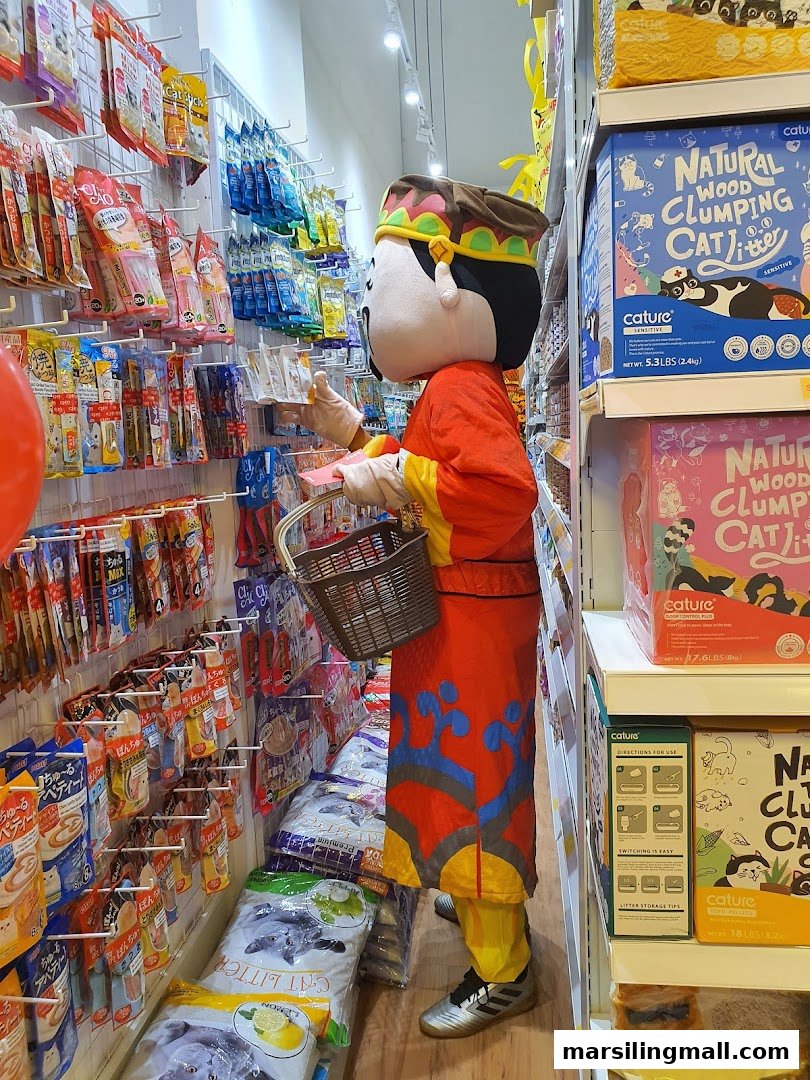 A mascot in traditional costume shops for pet supplies, browsing shelves in a well-stocked pet store.