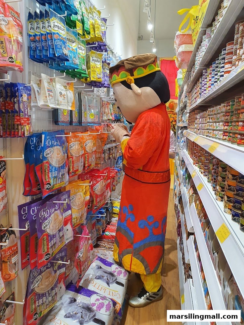 A mascot in a red costume browsing pet food and supplies on shelves inside Superpets store.