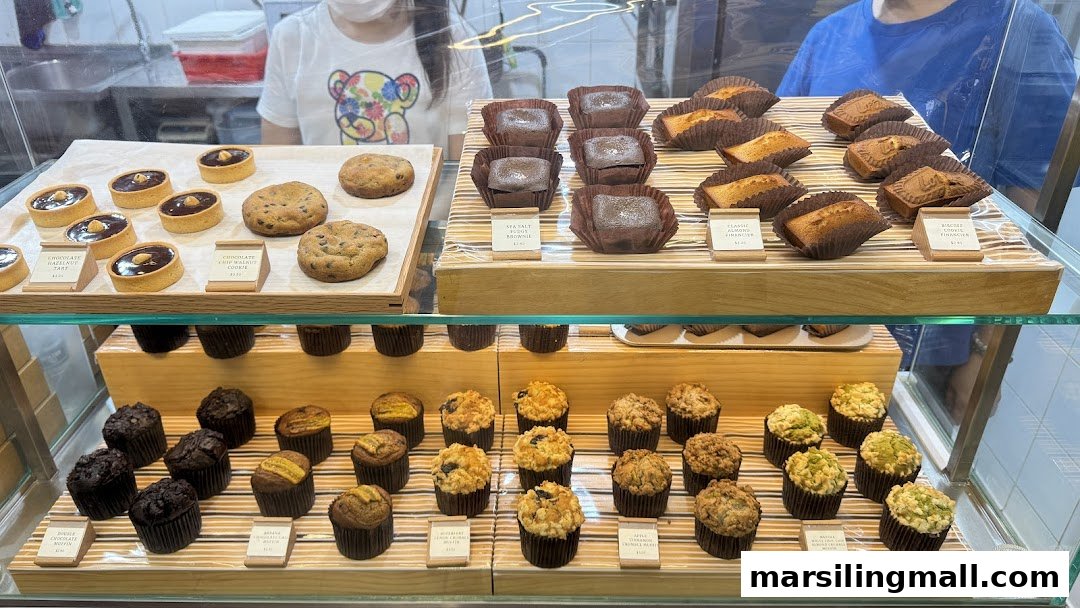 A vibrant display case showcasing a variety of freshly baked tarts, cookies, brownies, and muffins with price tags.