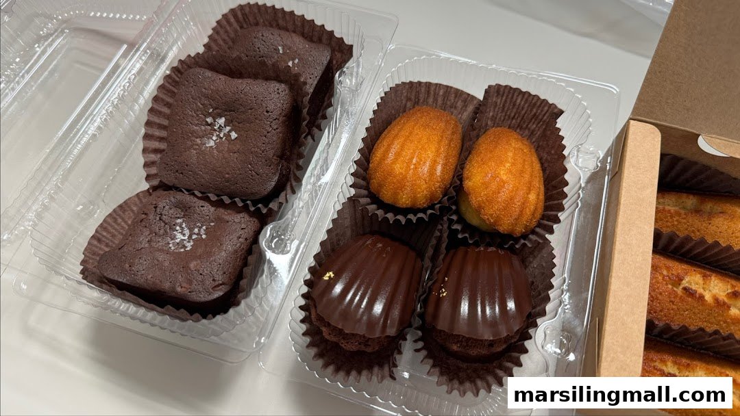 Assorted baked goods including brownies, madeleines, and chocolate shell cakes in clear and cardboard packaging.