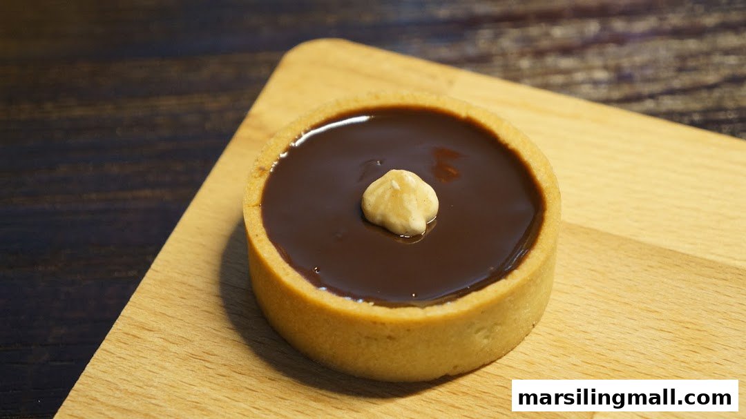 A delicious chocolate tart with a hazelnut on top, resting on a wooden board.