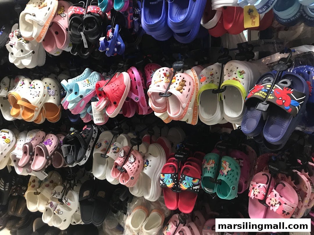 A vibrant display of various colorful children's sandals and clogs hanging in a retail store.