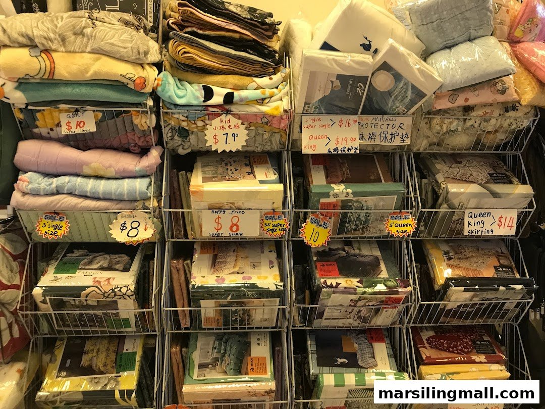 A retail display showcasing a variety of neatly stacked bedding, quilts, and mattress protectors in wire baskets.