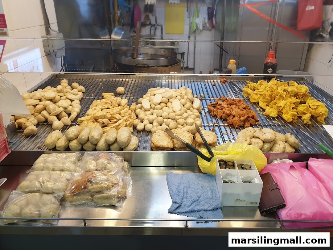 A display counter showcasing various fried fish balls, fish cakes, and crispy wontons at a food stall.