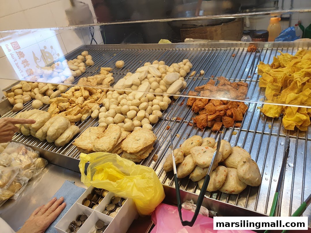 A variety of fresh fish balls, fish cakes, and fried wontons displayed in a food stall.