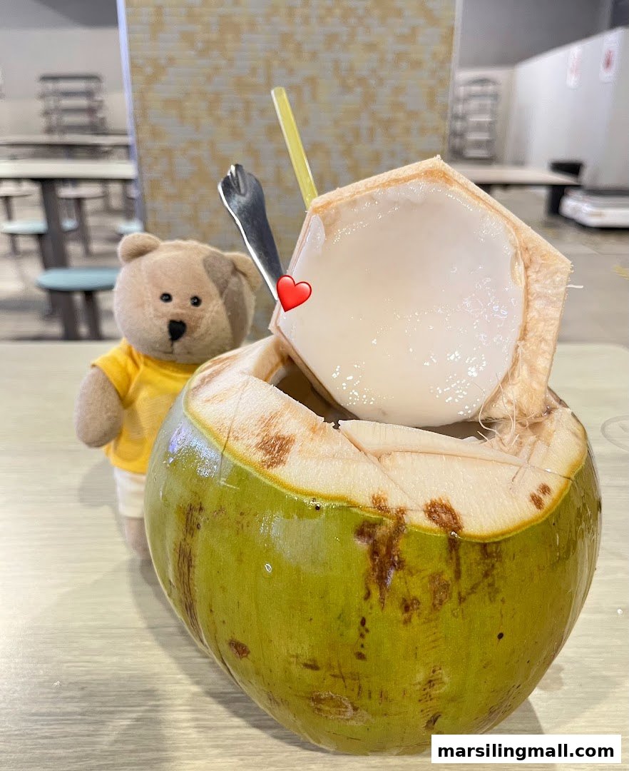 A fresh coconut drink with a spoon and straw, accompanied by a small teddy bear.