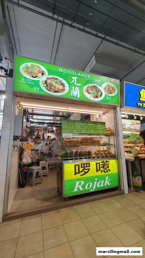 A vibrant food stall named Woodlands Rojak, showcasing its menu and fresh ingredients.