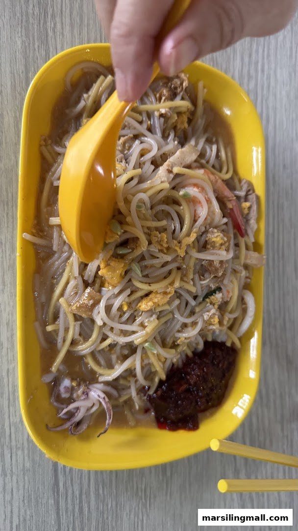 A vibrant yellow plate of stir-fried noodles with shrimp, squid, egg, and a dollop of chili paste.
