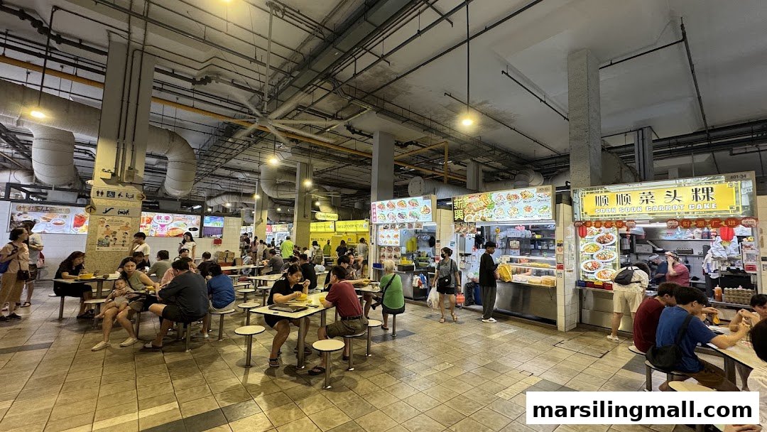 A bustling food court with multiple food stalls and diners enjoying various local dishes at tables.