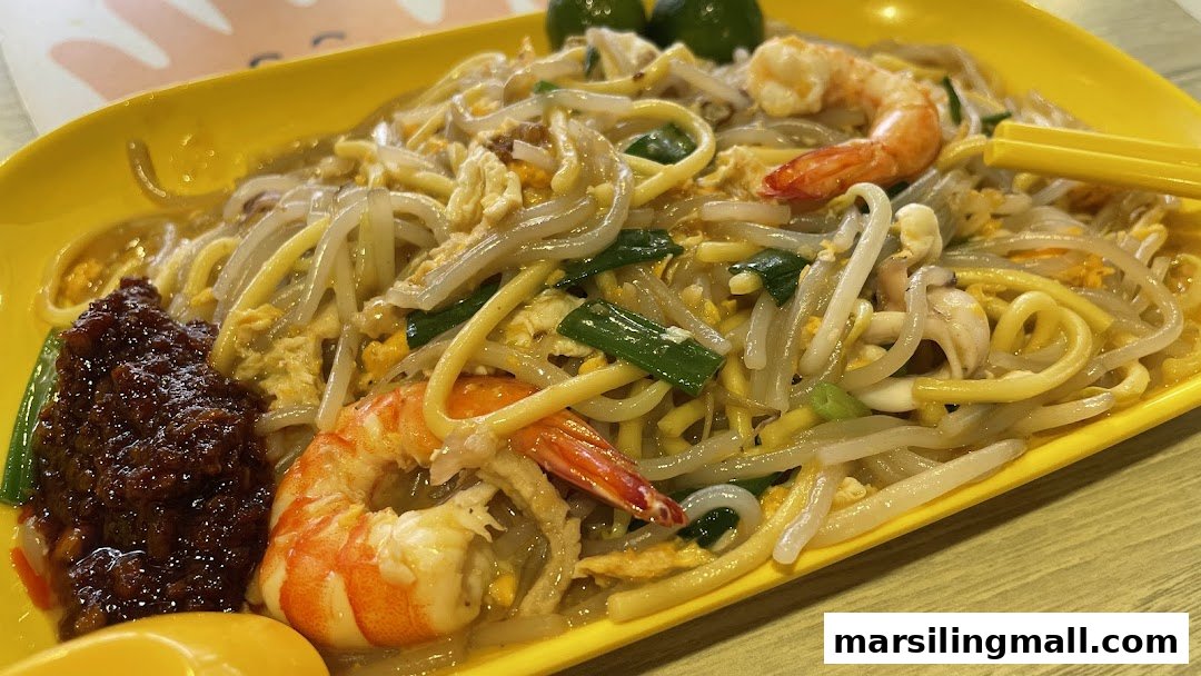 A vibrant plate of stir-fried noodles with prawns, squid, eggs, and a side of spicy chili paste.