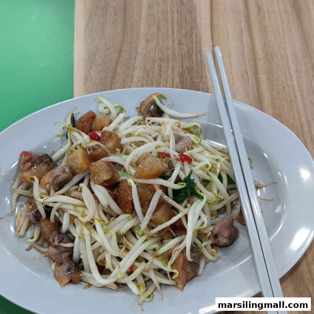 A close-up of a plate featuring stir-fried bean sprouts with crispy pork belly and cockles, served with chopsticks.