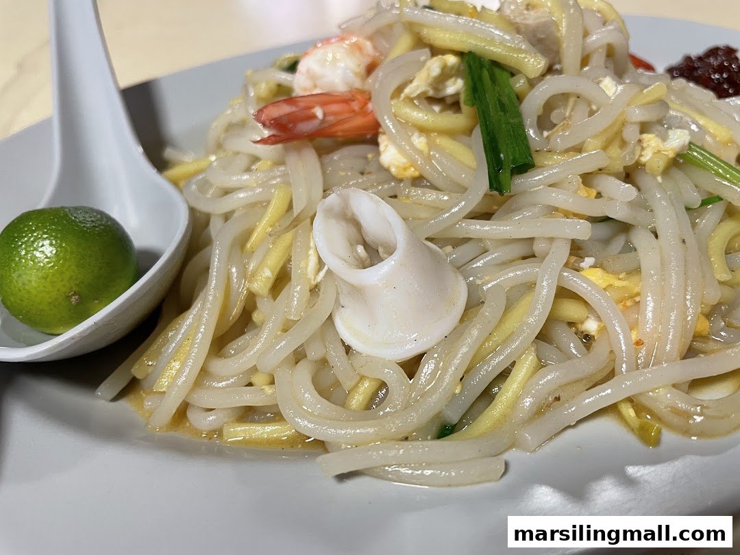 A close-up of a plate of stir-fried noodles with shrimp, squid, egg, and a lime.