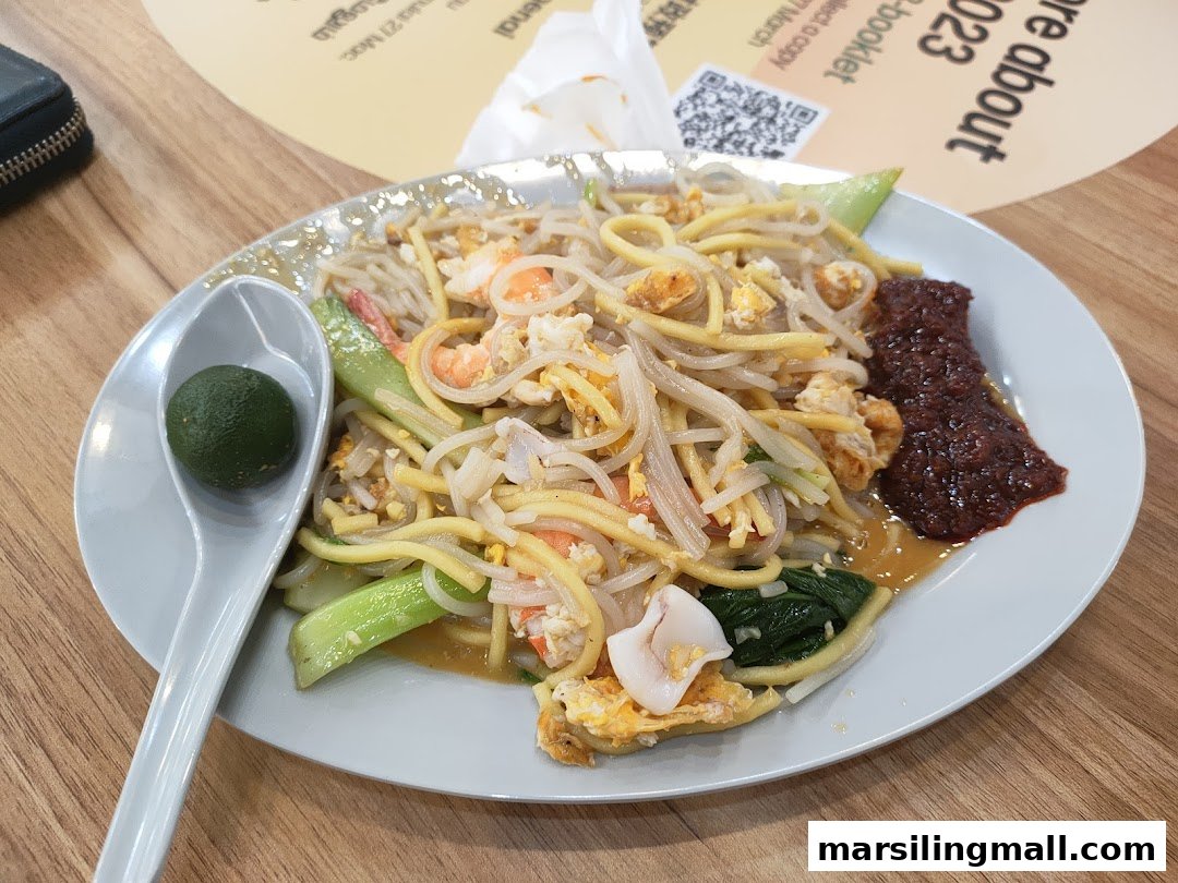 A plate of fried noodles with prawns, squid, vegetables, chili paste, and a lime.