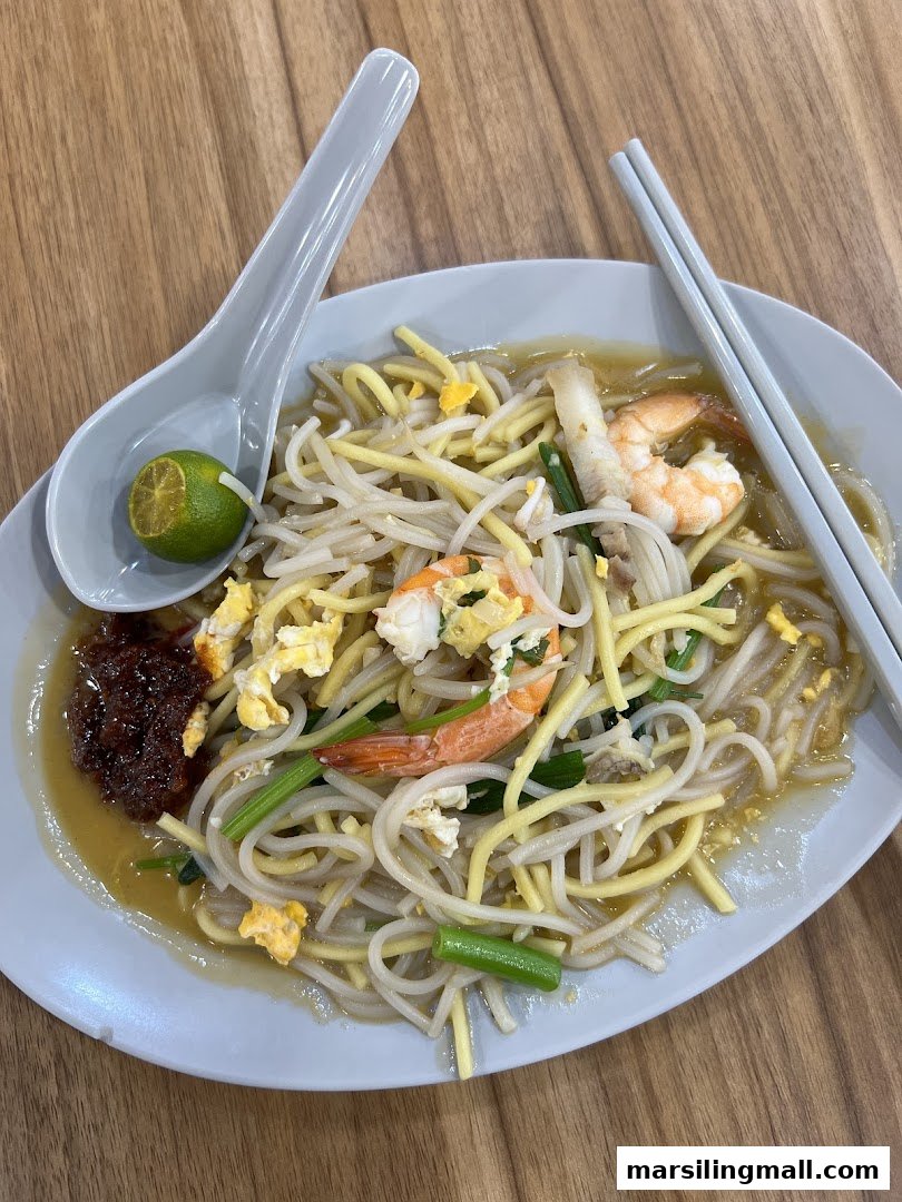 A close-up of a delicious plate of fried noodles with shrimp, egg, and vegetables, served with a lime and chili paste.