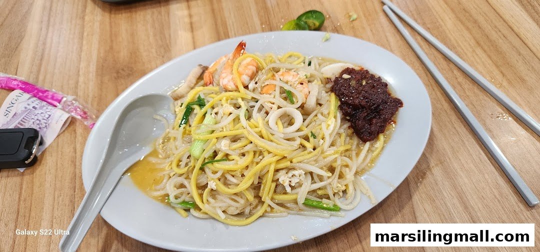 A close-up of a delicious plate of fried noodles with prawns, squid, and a dollop of chili paste.