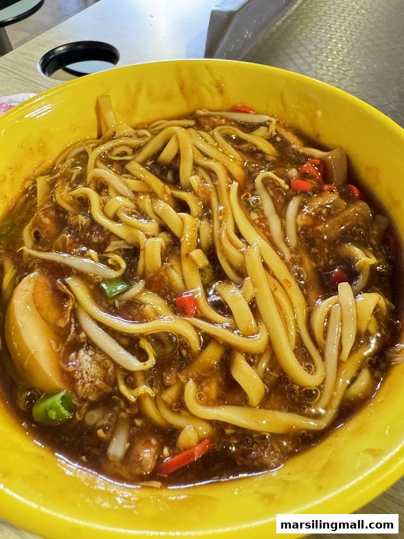 A vibrant yellow bowl filled with rich, savory laksa noodles, garnished with fresh ingredients.