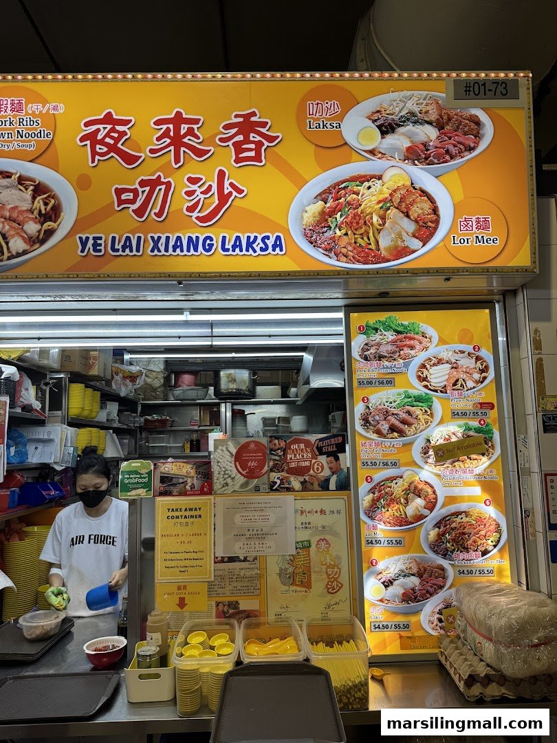 Front view of Ye Lai Xiang Laksa hawker stall, featuring staff, food displays, and a detailed menu board.