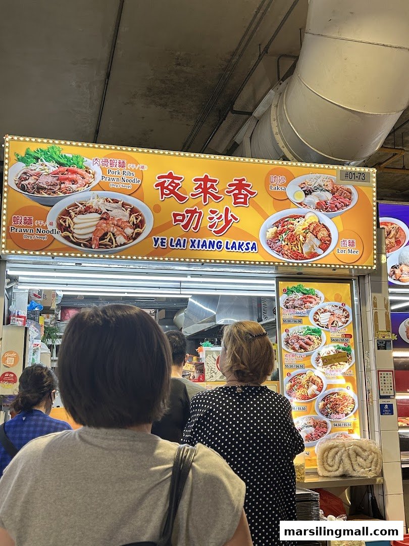 A vibrant food stall, Ye Lai Xiang Laksa, with customers queuing and a bright signboard showcasing its signature dishes.