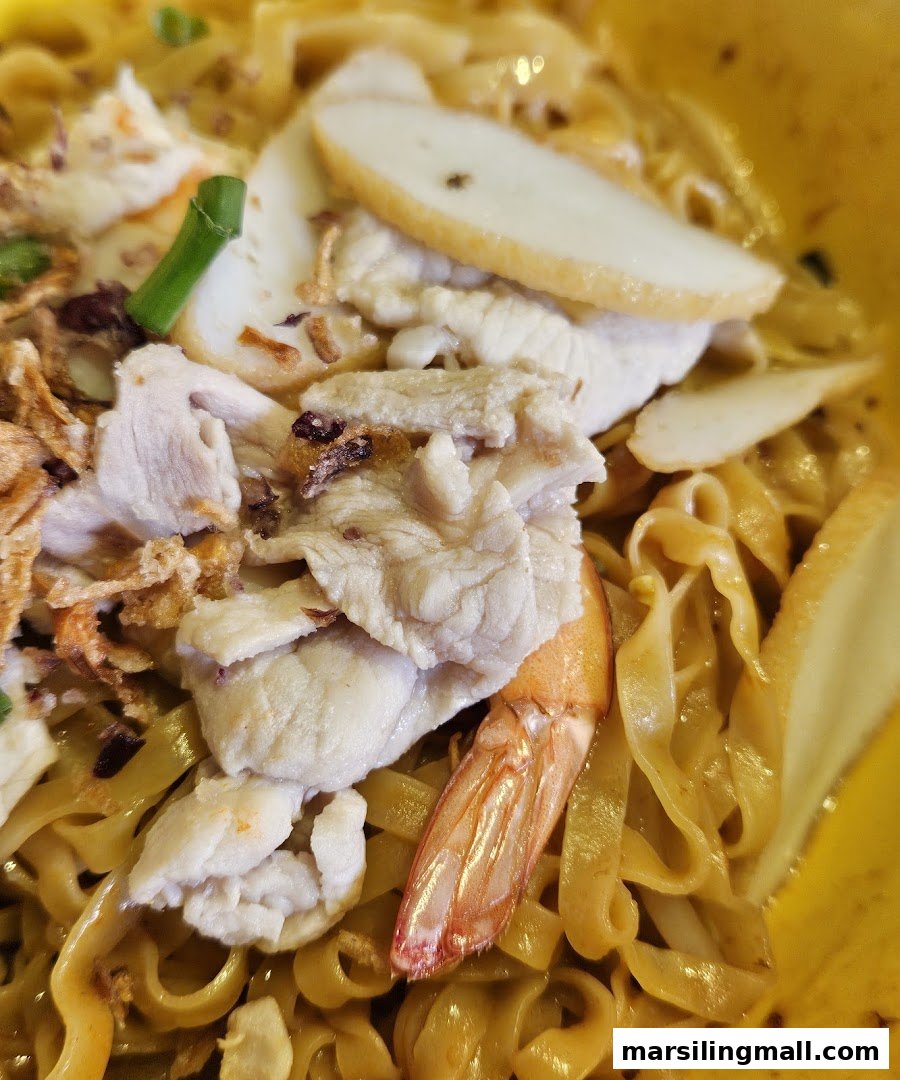 A close-up of a vibrant bowl of noodles topped with sliced meat, fish cake, and a prawn.