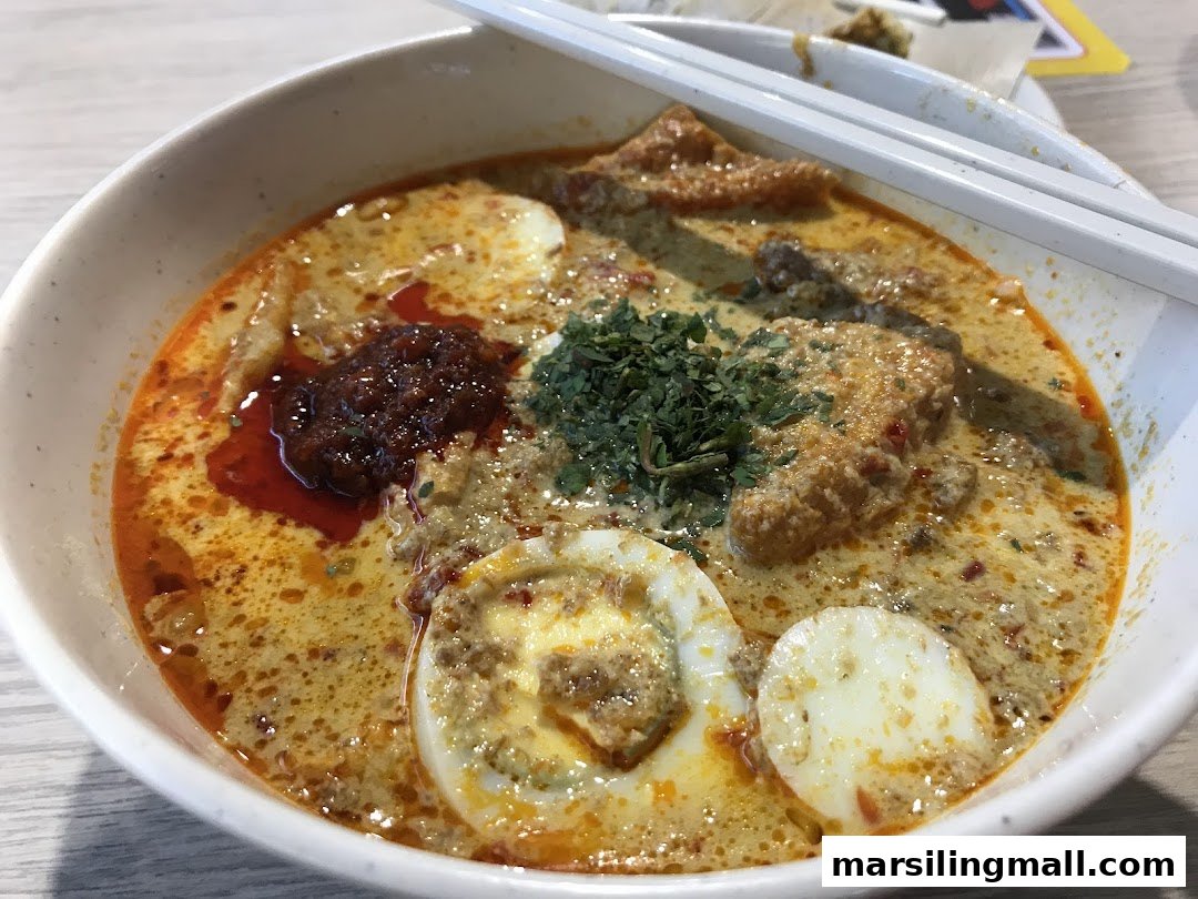 A close-up of a vibrant bowl of Laksa with rich broth, eggs, chili paste, and herbs.