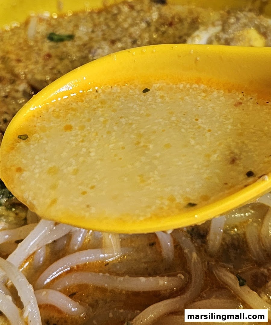 A close-up of a spoon scooping rich, flavorful laksa broth with noodles.