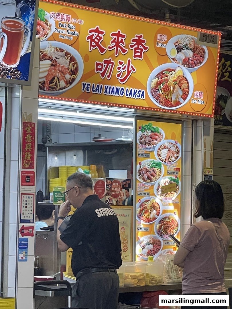 A bustling food stall counter at Ye Lai Xiang Laksa, featuring menu displays and customers.
