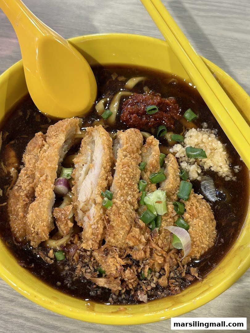 A vibrant yellow bowl filled with dark sauced noodles, crispy fried chicken, and fresh garnishes.