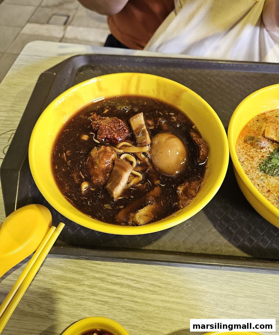 A close-up of a rich, dark braised noodle dish with meat and egg, alongside a partial view of a laksa.