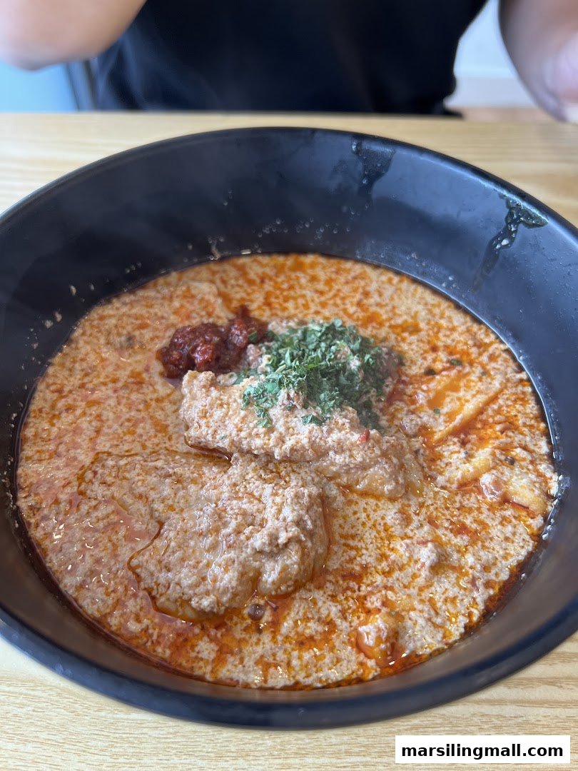 A close-up of a rich, creamy bowl of laksa with a dollop of chili paste and fresh herbs.