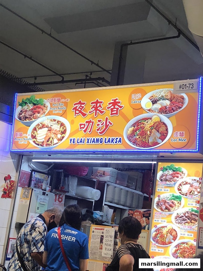 Brightly lit signboard of Ye Lai Xiang Laksa food stall with customers ordering.