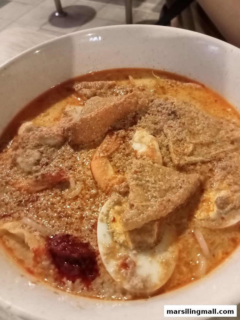 A close-up of a delicious bowl of Laksa with prawns, egg, and tofu puffs.