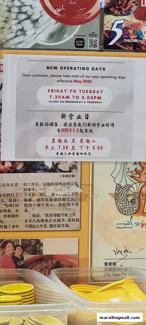 A notice board displaying new operating hours for Ye Lai Xiang Laksa, with kitchenware in the foreground.