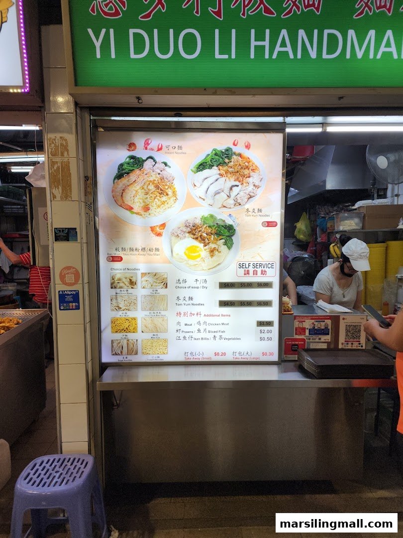 A noodle stall with a bright menu board showcasing various noodle dishes and ingredients.
