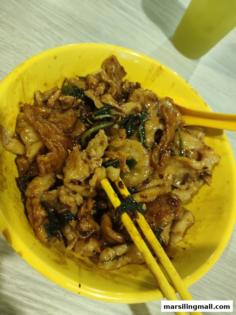 A close-up of stir-fried noodles with meat and greens in a vibrant yellow bowl with chopsticks.