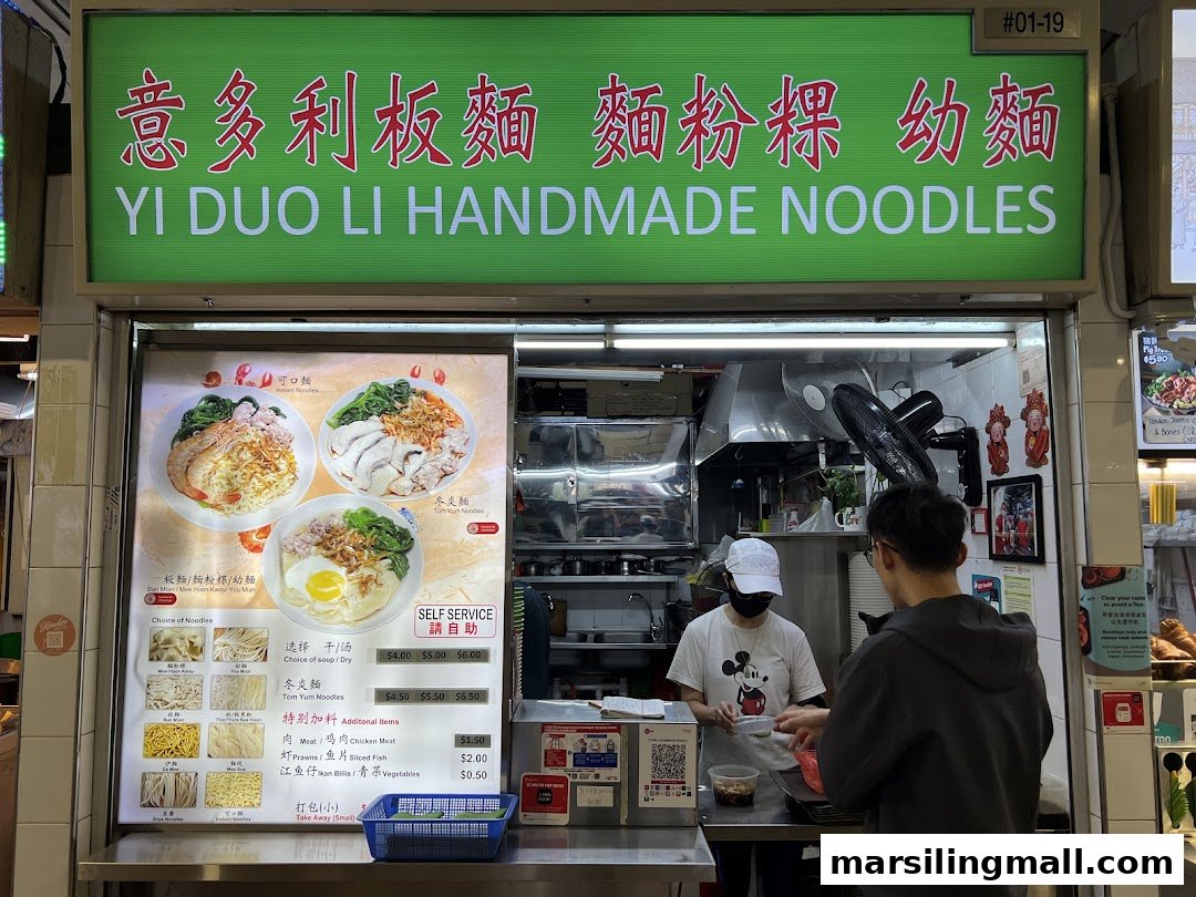 The front of 'Yi Duo Li Handmade Noodles' stall, featuring its signboard, menu board, and a customer ordering.
