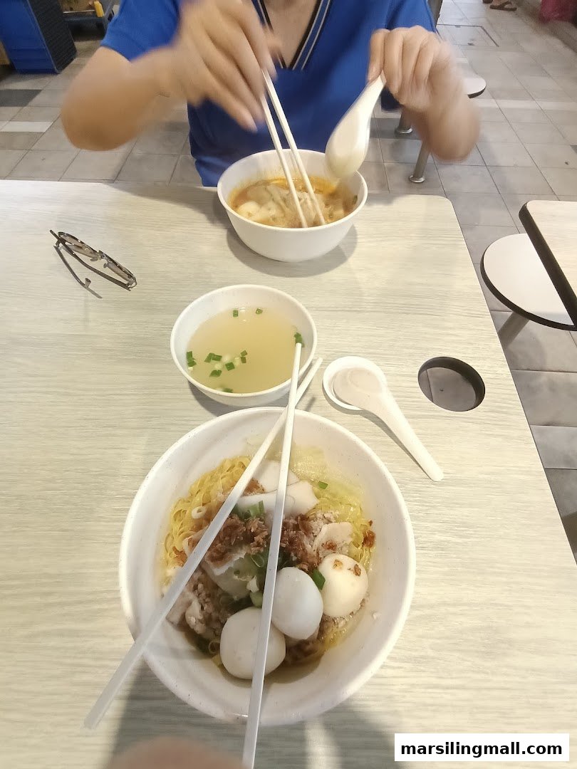 Two bowls of delicious minced meat fishball noodles and soup on a table, with a person enjoying a meal.